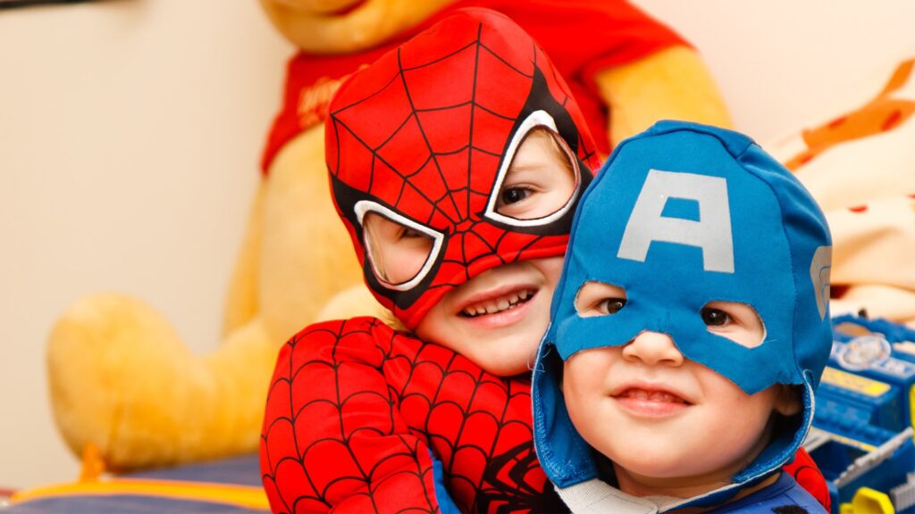 Zwei Kinder in Superhelden-Kostümen, Spider-Man und Captain America, lachen.