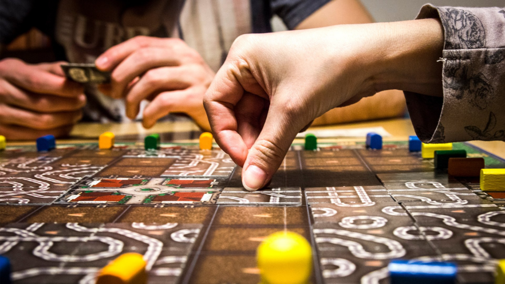 Hand bewegt Spielstein auf einem Brettspiel mit bunten Spielsteinen.