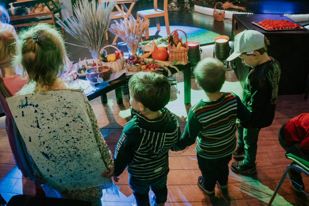 Vier Kinder stehen um einen Tisch mit Essen und Dekorationen bei einer Veranstaltung.