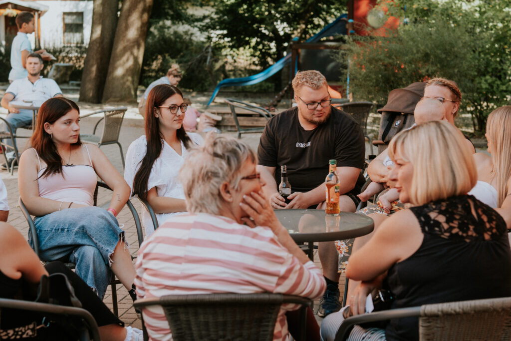 Mehrere Menschen sitzen im Garten an Tischen und unterhalten sich.