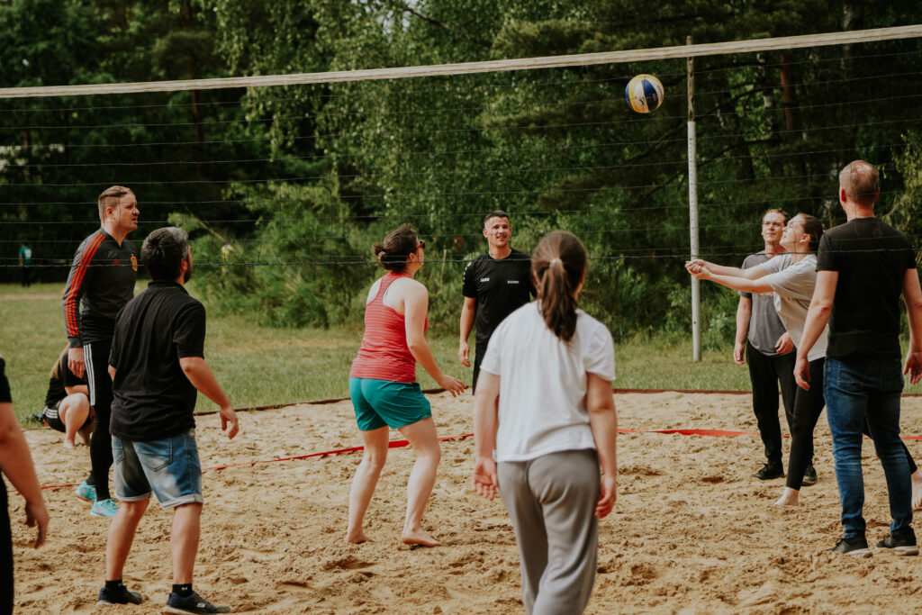 Mehrere Menschen spielen Volleyball auf einem Sandplatz im Freien.