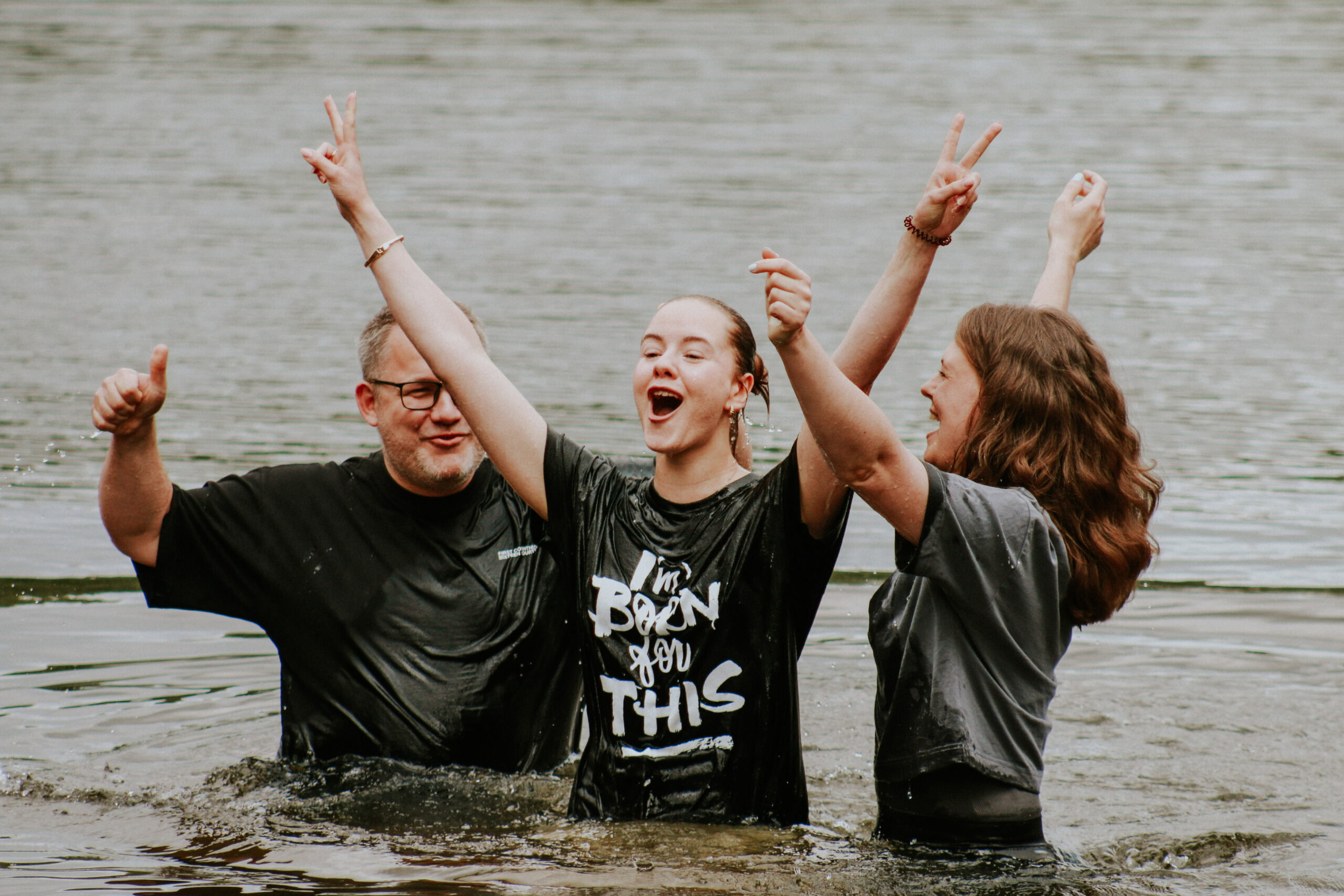 Drei Menschen stehen im Wasser, feiern und machen Peace-Zeichen.