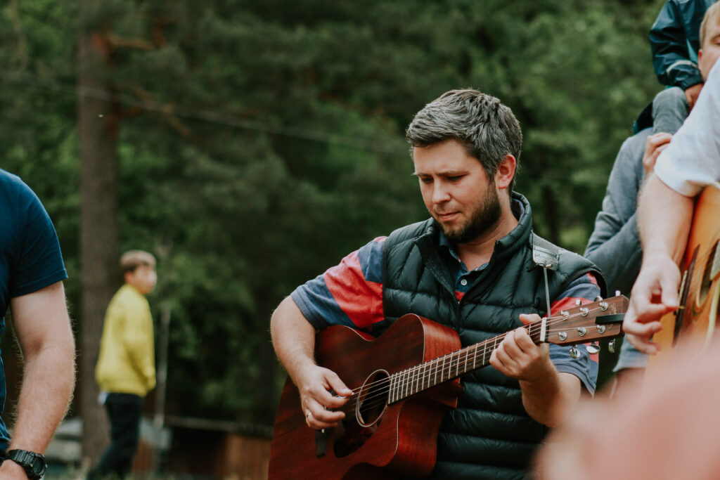 Mann spielt Gitarre im Freien, umgeben von anderen Personen.