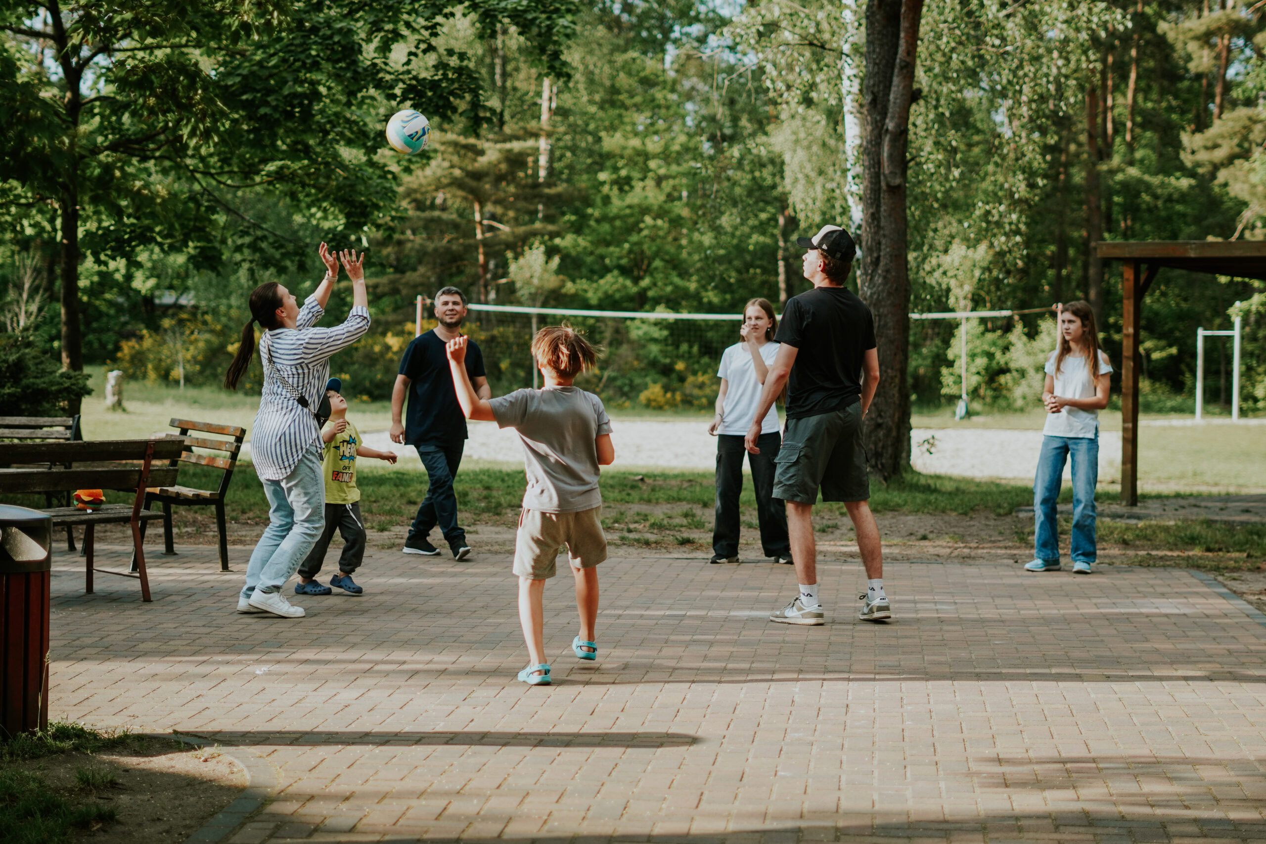 Menschen spielen Volleyball im Park, umgeben von Bäumen und Bänken.