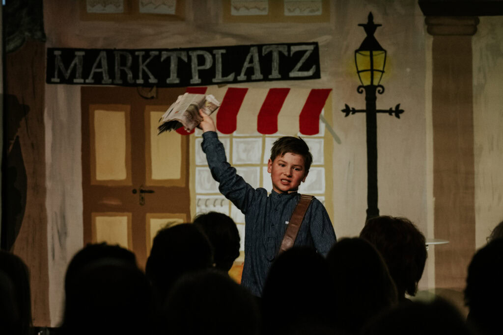 Junge Schauspieler liest aus einem Buch auf einer Bühne vor Publikum.