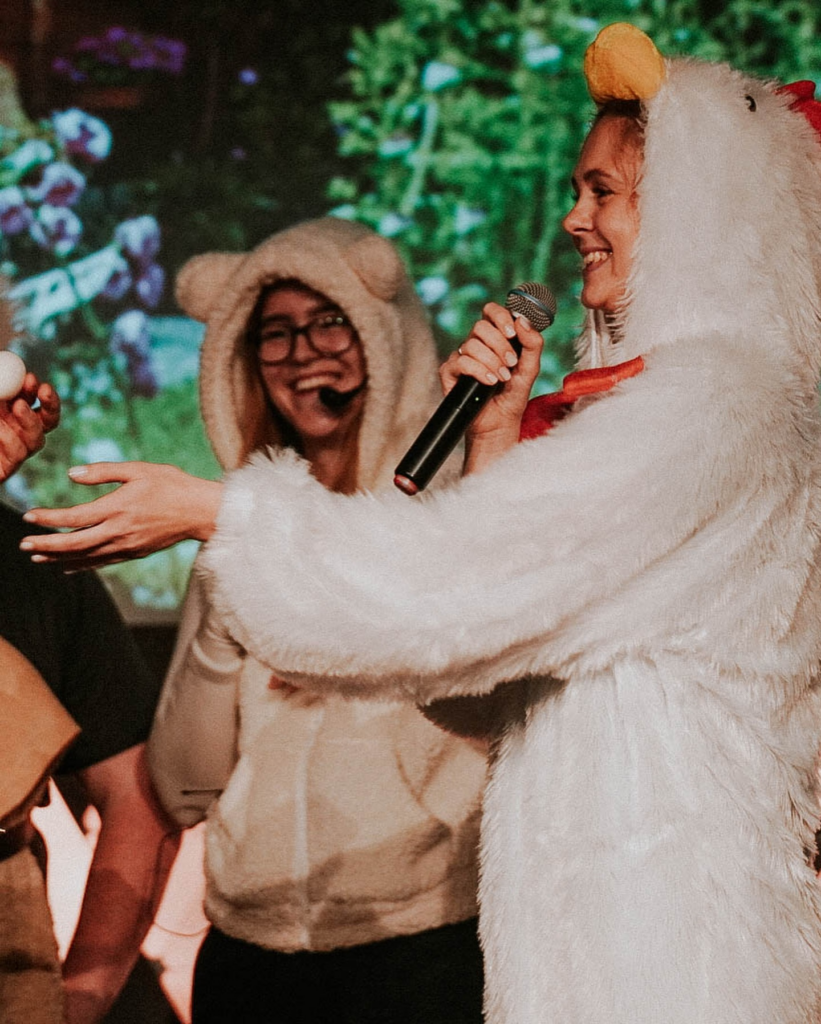 Zwei Menschen in Tierkostümen, einer hält ein Mikrofon, beide lachen.