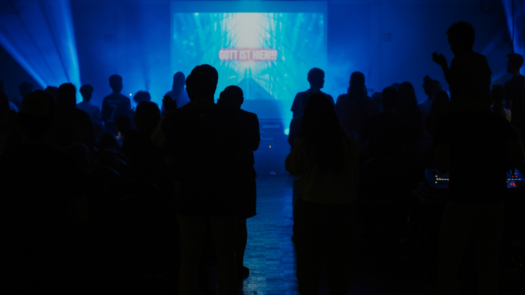 Menschen stehen in einem dunklen Raum vor einer großen Leinwand mit blauer Beleuchtung.