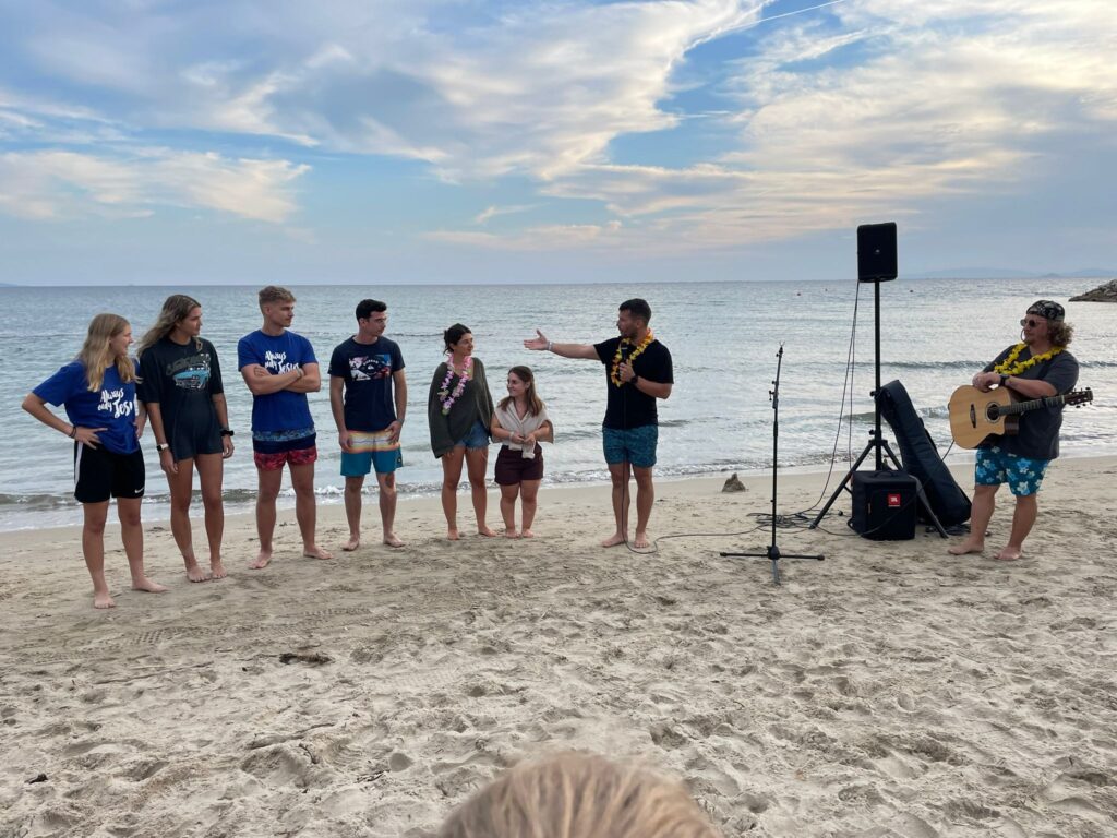 Jugendliche am Strand, einer spricht, ein Musiker spielt Gitarre.