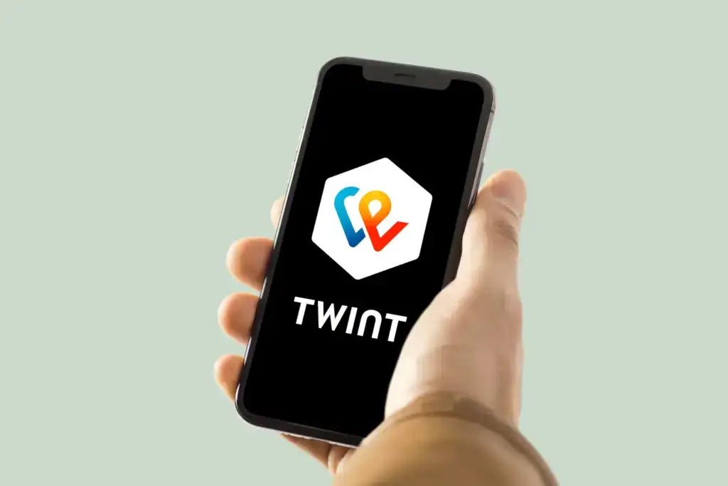 Hand hält Smartphone mit Twint-App-Logo auf schwarzem Hintergrund.