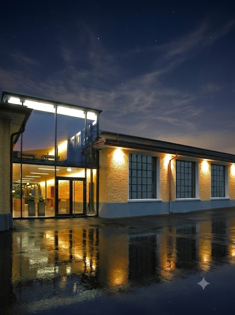 Gebäude bei Nacht mit beleuchteten Fenstern und reflektierendem Boden.