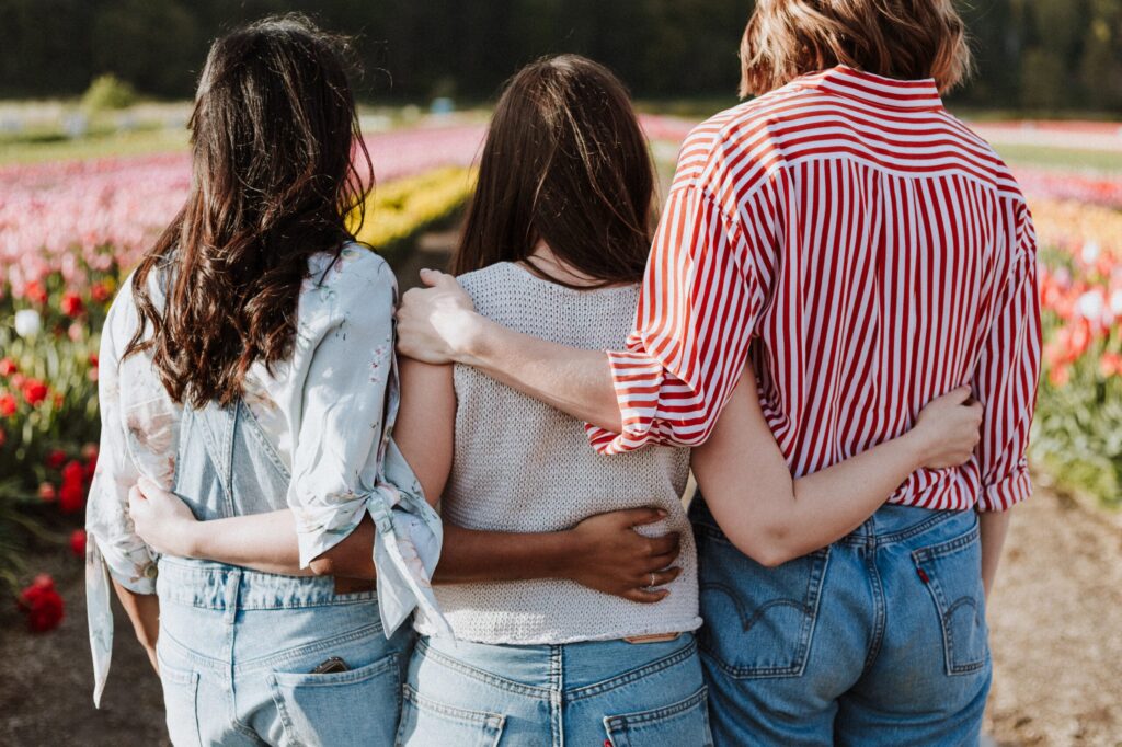Drei Frauen stehen in einem Blumenfeld, die Rücken sichtbar.