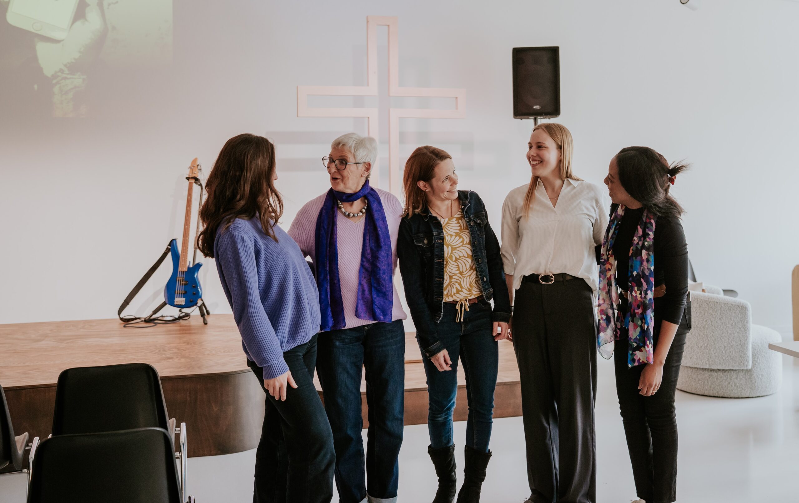 Fünf Frauen stehen im Gespräch in einem Raum mit einem Kreuz an der Wand.