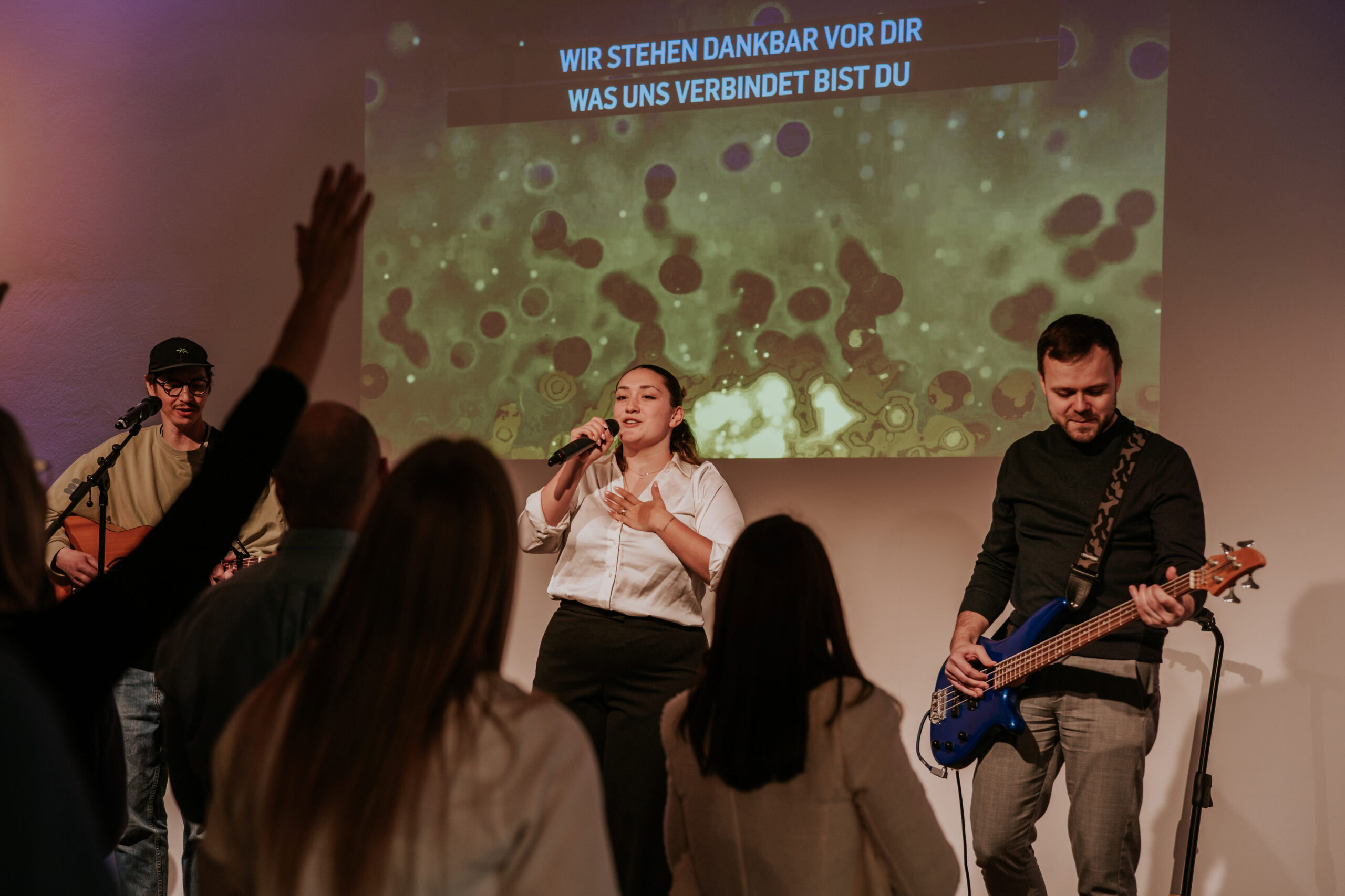 Frau singt mit Mikrofon, Gitarrist im Hintergrund, Publikum im Vordergrund.