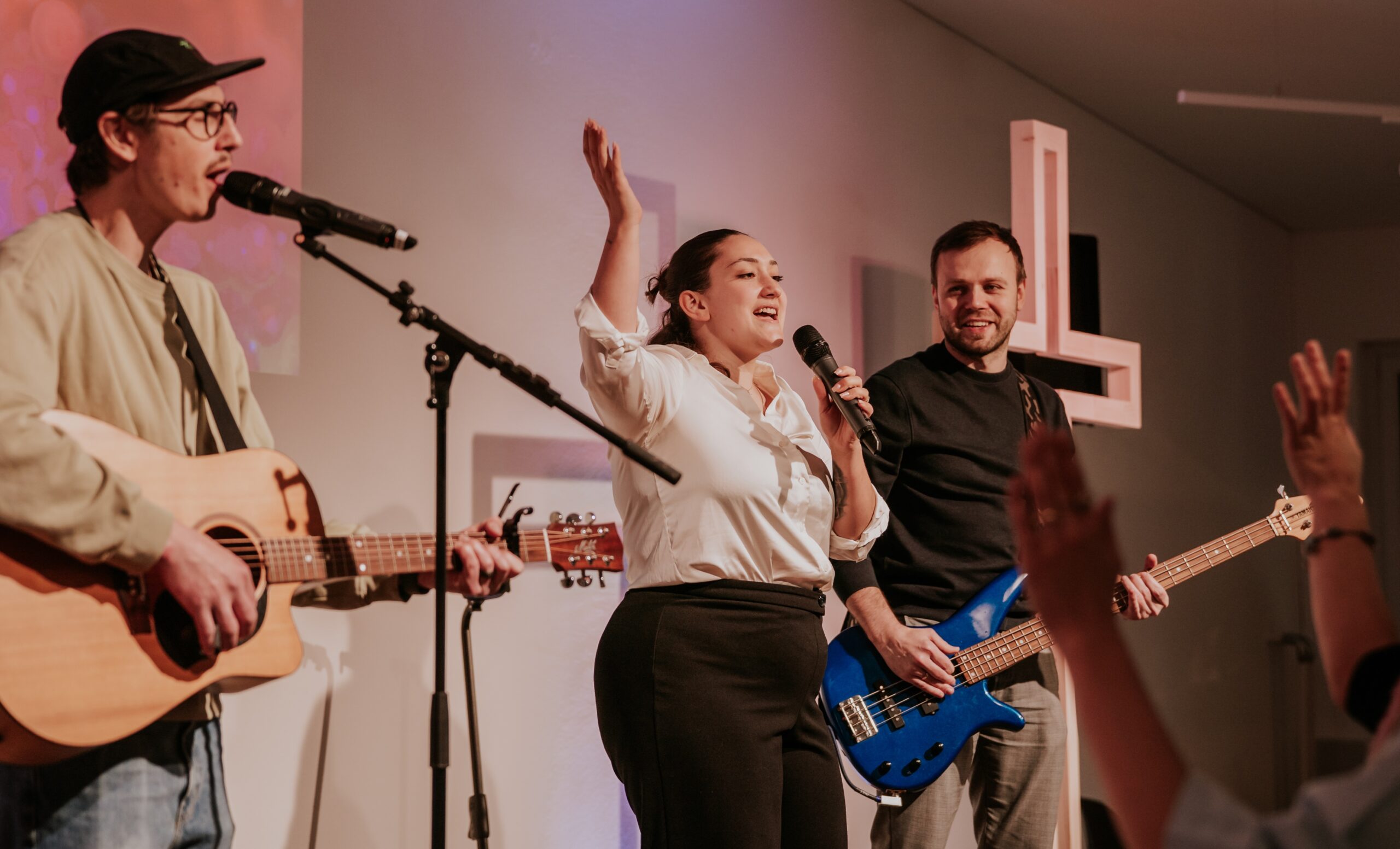 Drei Musiker auf Bühne, einer singt, zwei spielen Gitarre, Publikum hebt Hände.