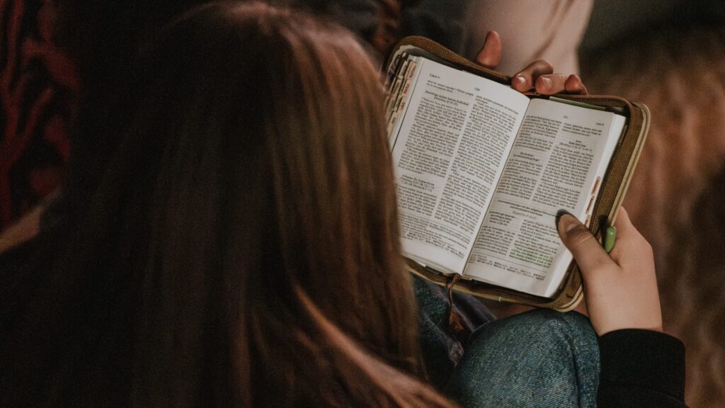 A person reading the Bible in a group, with a candle visible in the background.