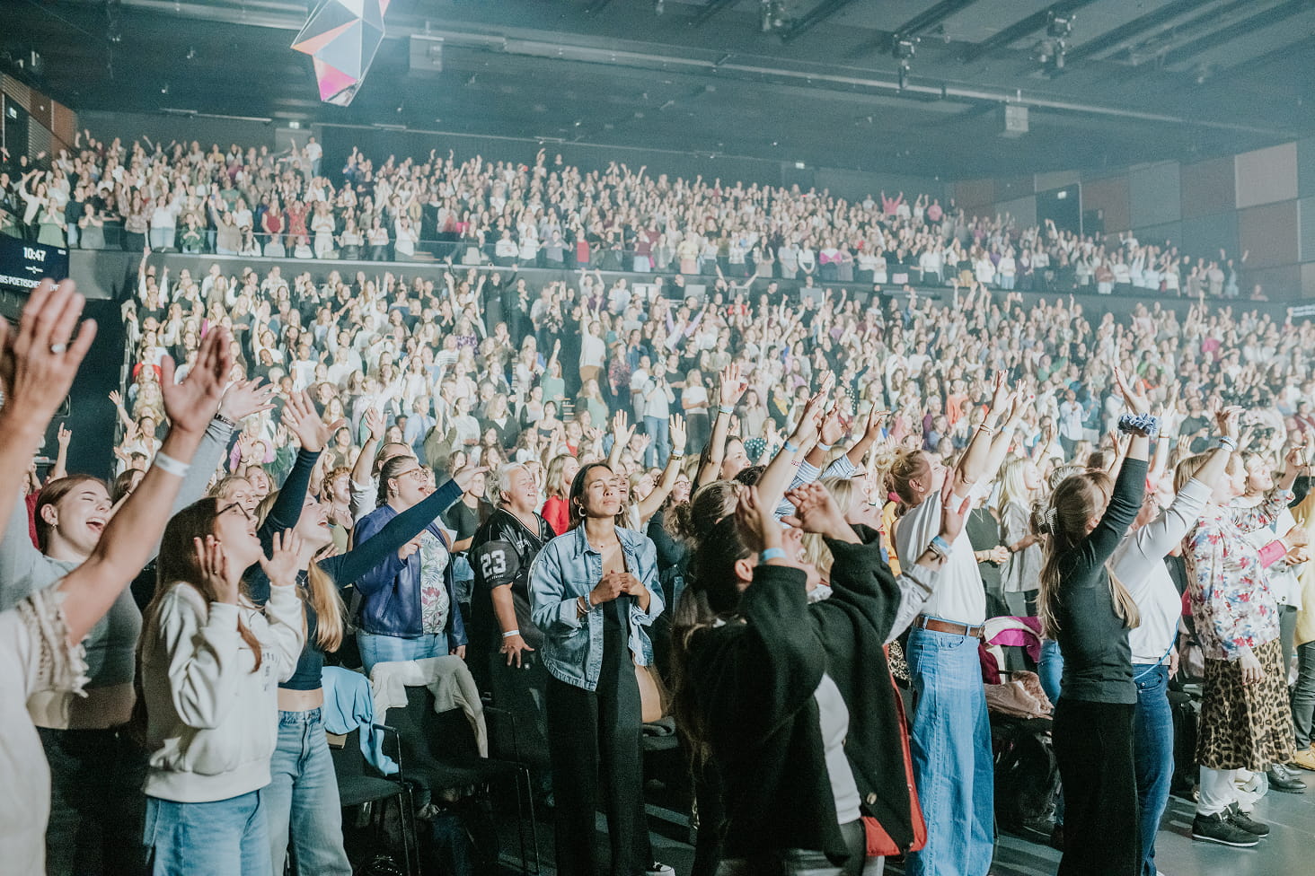 Menschen in einem grossen Saal heben die Hände in die Luft.