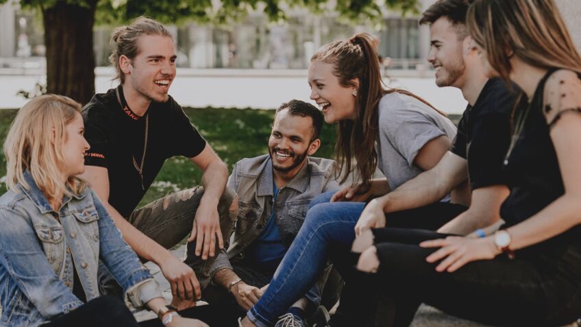 Sechs junge Menschen sitzen im Park und unterhalten sich.