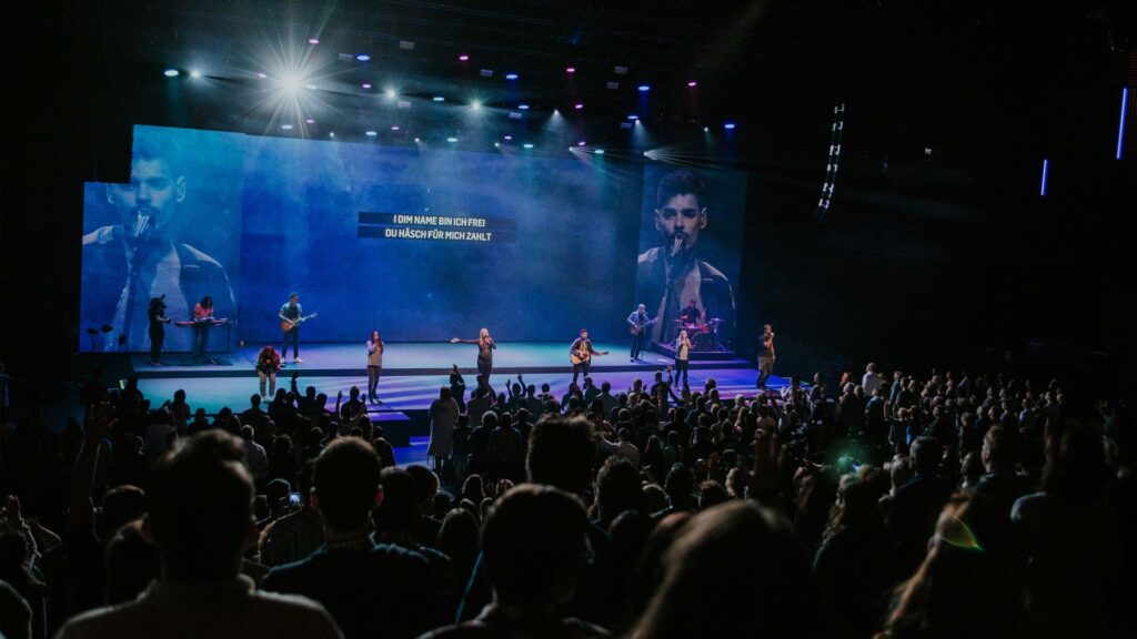 Musicians on a stage at a concert, large screen in the background.