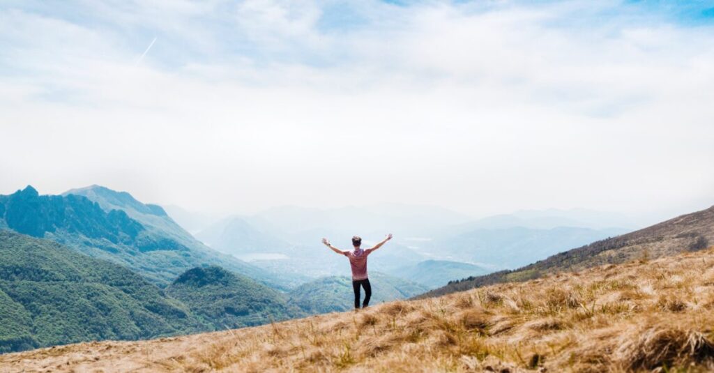 Person auf Bergkamm mit ausgebreiteten Armen