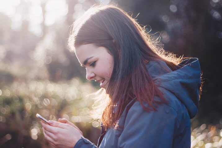 Junge Frau schaut auf ihr Smartphone im Freien bei Sonnenlicht.