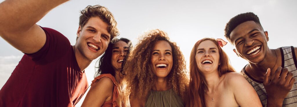 Fünf junge Menschen lachen und posieren im Freien bei Sonnenlicht.